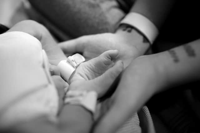 Tia holding her son JJ’s feet after he was stillborn in February 2026.