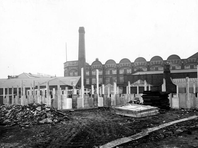 Wooden posts, concrete slabs and a pile of stones are visible. Wm. Blackburn and Co. Ltd. clothiers can be seen in the background on Springwell Road, Holbeck.