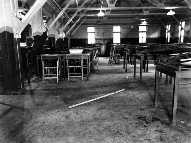 The dining area of the British Restaurant at Sheepscar. A self-service counter is to the left, with plain wooden tables and foldaway chairs on the right.