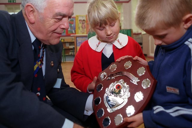 Pupils from Barley Hill Infants School study The Hammond Shield awarded to them by Michael Hammond of The Royal British Legion for selling the most poppies per head in Garforth.