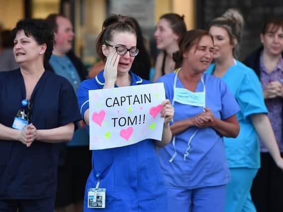 An NHS staff member wipes her eyes as she holds a sign to thank British veteran Captain Tom Moore who raised over 13 million GBP for the NHS as they take part in a national "clap for carers"