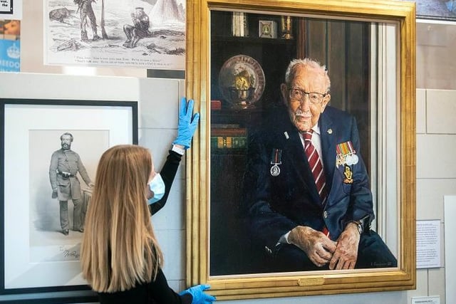 A staff member adjusts a portrait of Captain Sir Tom Moore by artist Alex Chamberlin, as it is unveiled at the National Army Museum in Chelsea, London to mark the 75th anniversary of VJ day