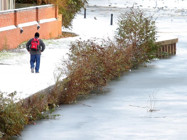 A man walks alongside the partially-frozen River Nene
