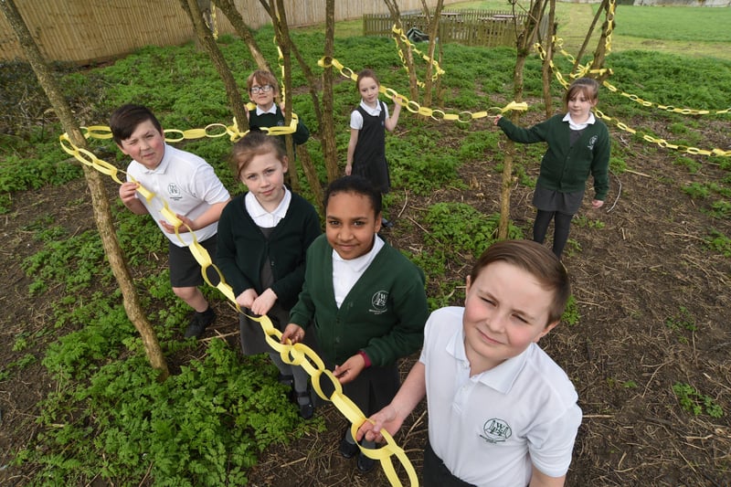 Pupils at Woodston primary school hanging yellow paper chains around  trees on the school field to remember one year since the first Covid 19 lockdown. EMN-210323-153045009