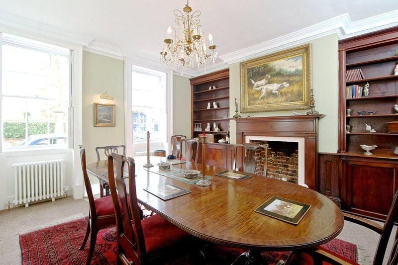 The dining room has two matching windows to the front with original shutters. There is a brick fireplace with a mahogany surround and mantel, a marble hearth, and mahogany shelving and cupboards in the alcoves on either side.