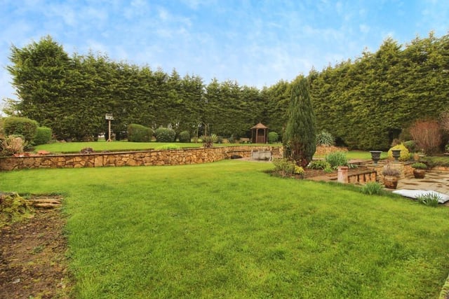 The attractive gardens feature well-maintained lawns, surrounded by trees.