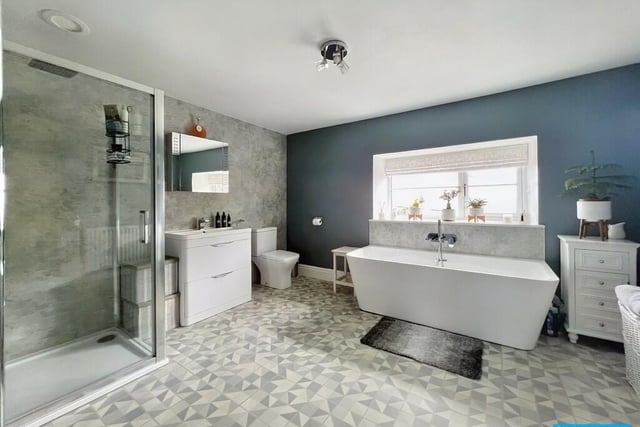 A contemporary double-ended bath takes pride of place in the family bathroom. There is a shower cubicle with overhead shower and handheld  shower sprays. The hand basin has an illuminated mirror above.