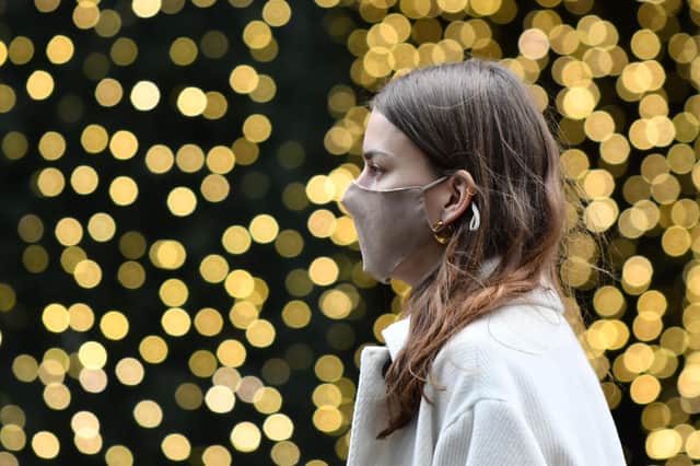 A pedestrian wearing a face mask walks past a Christmas light display  (Photo by JUSTIN TALLIS / AFP)