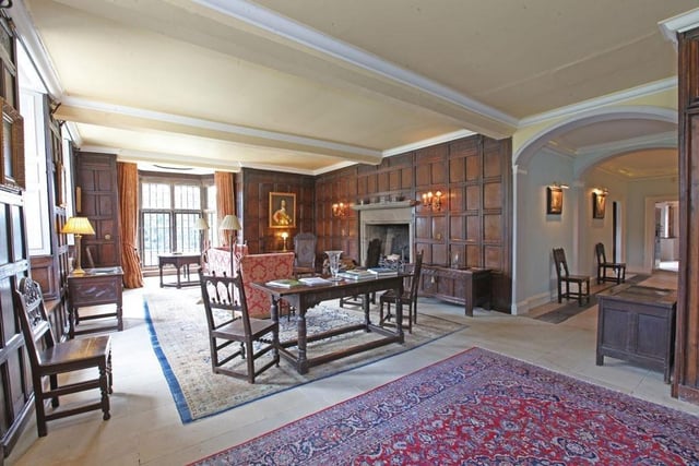 A large oak panelled  drawing room with open fireplace set in fossil marble surround, there is a bay window at the front and windows with built in seating overlooking the side garden and driveway.