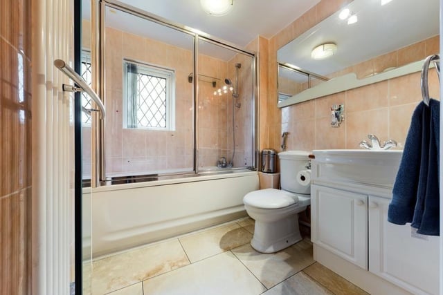 The family bathroom contains a bath with overhead shower which is enclosed by a screen and a vanity unit with storage beneath the basin.