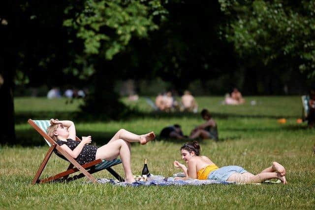 People sit on the grass in the sunshine. Photo by TOLGA AKMEN/AFP via Getty Images