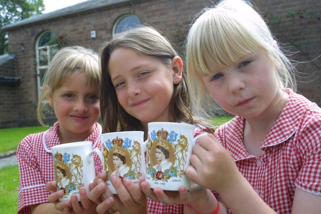 School children hold up their Queen's Golden jubilee celebration mugs in 2002