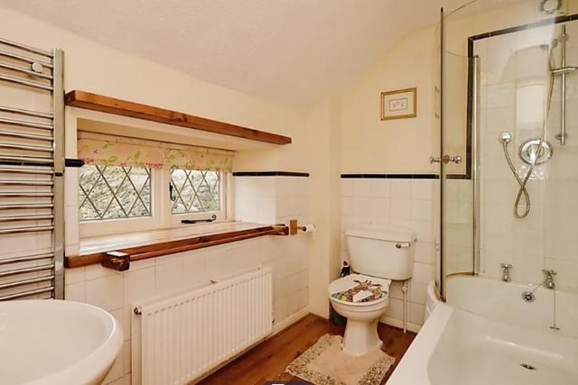 A bathroom suite in white includes bath with overhead shower and screen,  wash basin and wc.