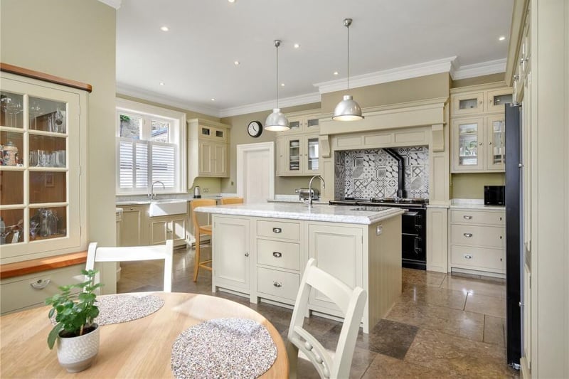 Shaker-style cabinetry is topped by marble worktops while an island features an inset sink and a breakfast bar for occasional seating. Integrated appliances include a four oven gas Aga, a dishwasher, a two-ring induction hob and a single electric oven.