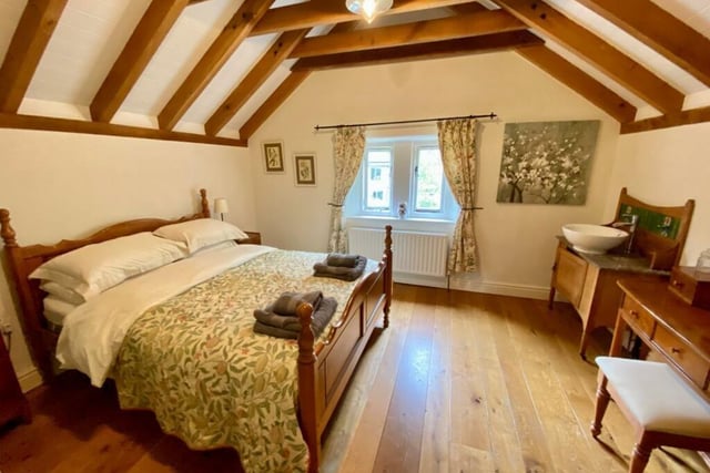This delightful double bedroom has an eye-catching open vaulted ceiling. A wash basin sits on top of a vanity unit.