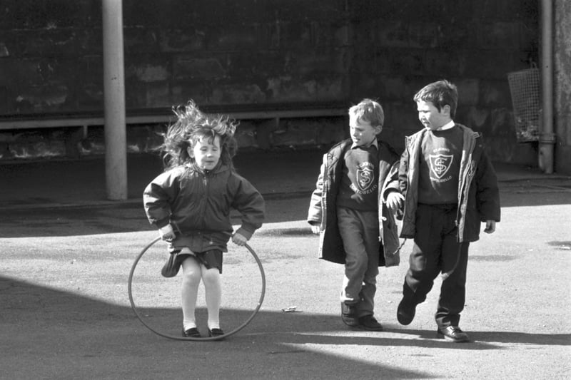 Two little boys watch a girl playing with her hoop in the playground of St John's RC primary school in Edinburgh, April 1989.