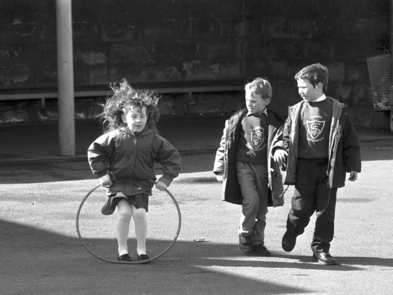 Two little boys watch a girl playing with her hoop in the playground of St John's RC primary school in Edinburgh, April 1989.