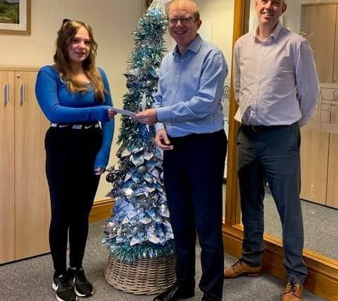 Mya is presented with a Hobbycraft gift voucher as part of her prize by Steve Taylor, director of Start Financial Planning, watched by Graeme Goodwin, a paraplanner.