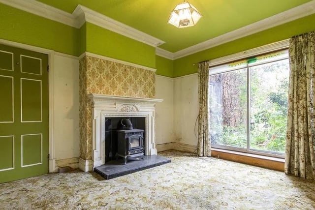 A solid fuel heater stands on a tiled hearth in a fireplace with ornate surround. The room has original picture rail and coving. Sliding patio doors open onto the rear garden.