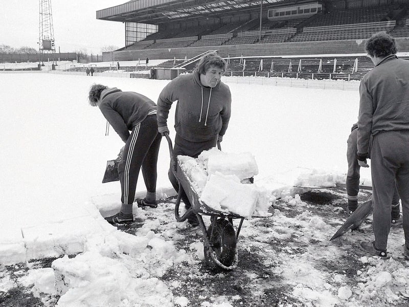 Stags players and staff clear snow from the pitch at Field Mill.