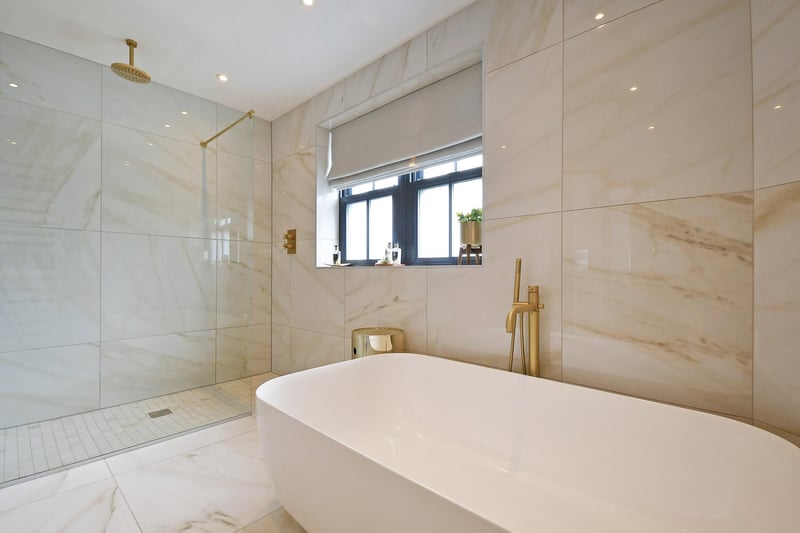 This fully tiled marble suite comprises a wall-mounted Duravit WC and a wall-mounted vanity unit, incorporating a timber work surface, storage beneath and two wash hand basins. There's a freestanding bath and a hand shower facility, a large walk-in shower as well as a built-in ceiling speaker and a Zehnder heated towel rail.