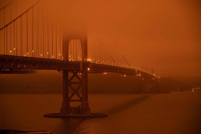Cars drive along the San Francisco Bay Bridge under an orange smoke filled sky at midday in San Francisco.