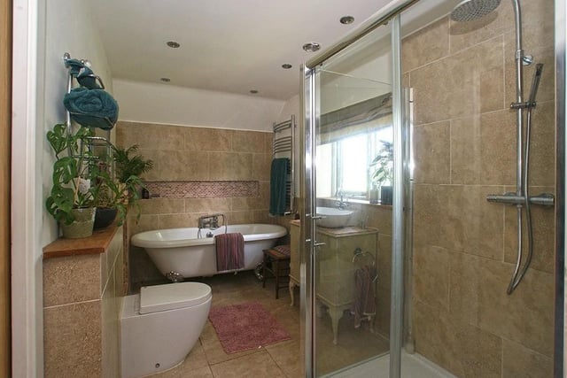 The partially-tiled room contains an antique-effect washstand with contemporary hand basin, a rolltop bath standing on ball and claw feet, a shower cubicle and a wc.