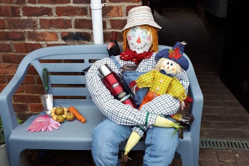 Sitting comfortably is this scarecrow with a flask and baby scarecrow.