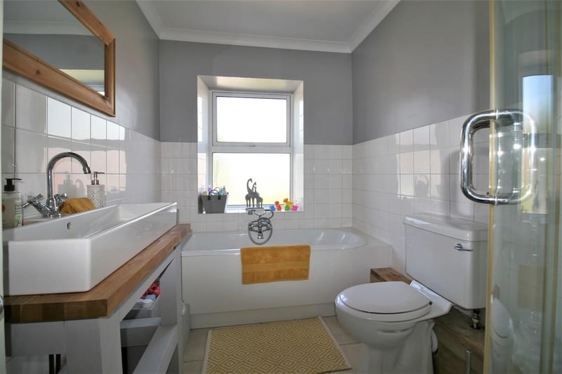 The bathroom has a shower, bath and sink with vanity unit.