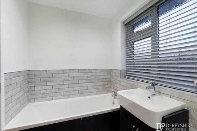 The bathroom also includes this panelled bath with hot and cold mixer tap, plus wood-effect laminate flooring, inset ceiling spotlights, an extractor fan and a chrome ladder-style central heating radiator/towel rail.