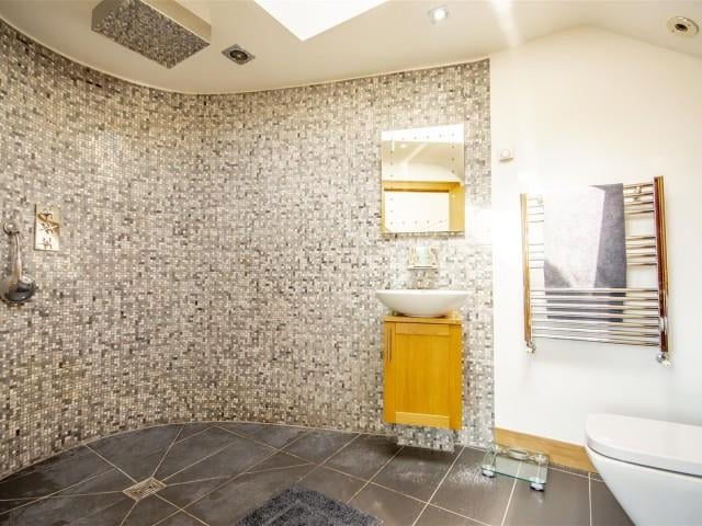 The en-suite has a low level flush WC, a counter-top wash basin with a base cupboard, a walk in rain shower with chrome fittings, an extractor fan, tiled flooring with underfloor heating, partially tiled walls, a chrome heated towel rail, built in cupboards, recessed spotlights and a Velux window.