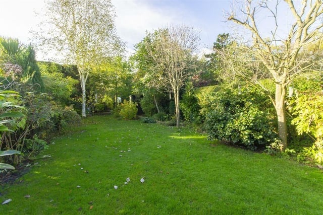 The rear garden includes a stretch of lawn with mature borders of plants, shrubs and trees.