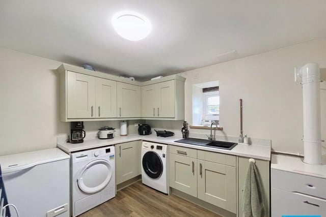 Painted wood storage units similar to those in the kitchen are fitted below a granite-style work surface with space for a washing machine and a tumble dryer.