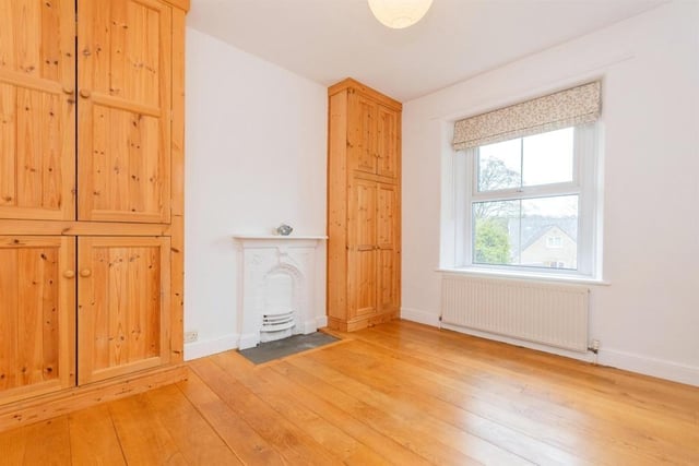 A period fireplace is the focal point of this room which has storage cupboards and a wooden floor.