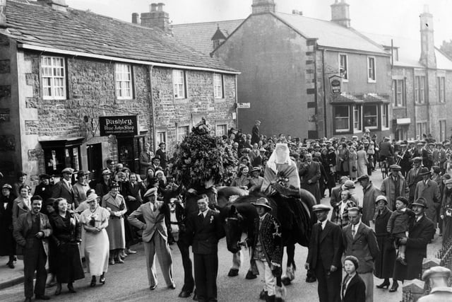 1 June 1936:  Garland day at Castleton. A veiled woman on a horse is led through the streets by a man in an embroidered coat. Another horse carries a huge garland.  (Photo by Fox Photos/Getty Images)