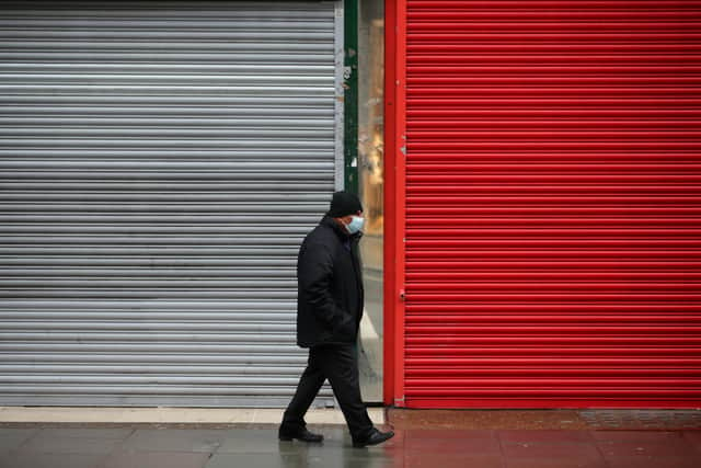 A man wearing a face mask walks past the shutters of temporarily-closed stores (Photo by David Cliff/NurPhoto via Getty Images)