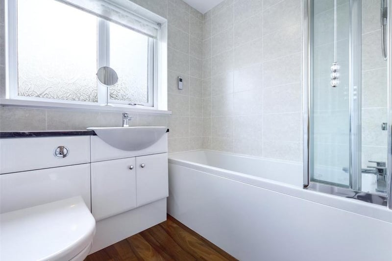 Family bathroom - Modern white suite comprising low level WC with concealed cistern, inset wash basin with vanity cupboard and panelled bath with mixer shower over; uPVC double glazed window to the rear elevation, tiled walls, wood effect laminate flooring and towel radiator.