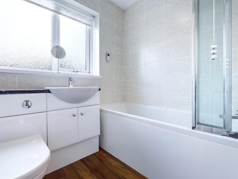 Family bathroom - Modern white suite comprising low level WC with concealed cistern, inset wash basin with vanity cupboard and panelled bath with mixer shower over; uPVC double glazed window to the rear elevation, tiled walls, wood effect laminate flooring and towel radiator.