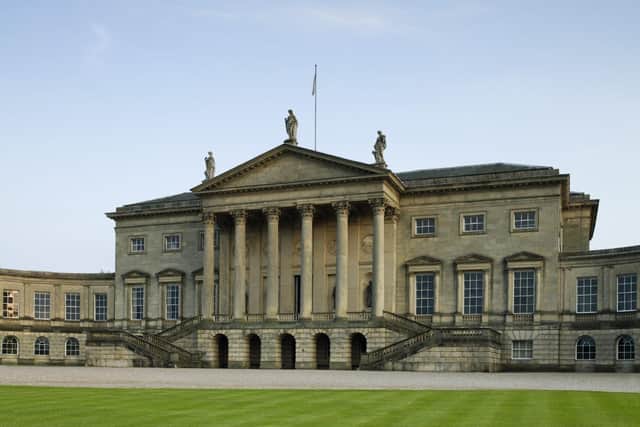 The north Palladian front of Kedleston Hall has classical sculptures and curved corridors leading to rectangular pavilions on either side.