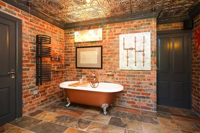 The magnifcent claw foot bath mounted on a rustic looking tiled floor is set against exposed brickwork. A  wall-mounted radiator and artwork give the room an industrial feel.