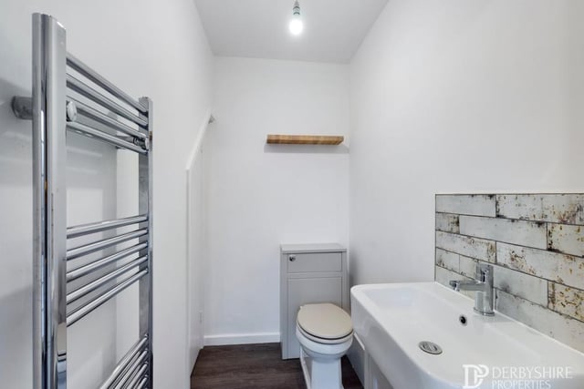 Here is the downstairs toilet or guest WC. It comprises a low-flush WC and wash hand basin with vanity unit, mixer tap and splashback tiling. Not to mention a laminate wood-effect floor and a chrome ladder-style central heating radiator/towel rail