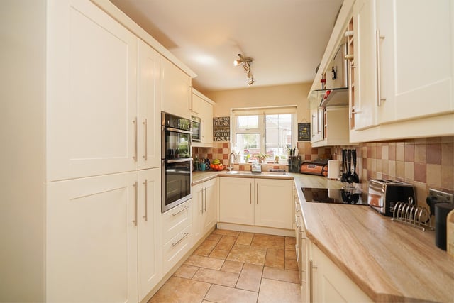 This welcoming  kitchen has  light coloured fitted wall and base units complemented by wood-effect work surfaces and tiled splashbacks and flooring.