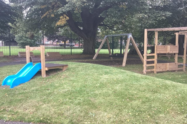 The green area at the back of the school building is sheltered by trees and includes a sandpit, a swing, a slide, and a climbing frame to promote physical activity.