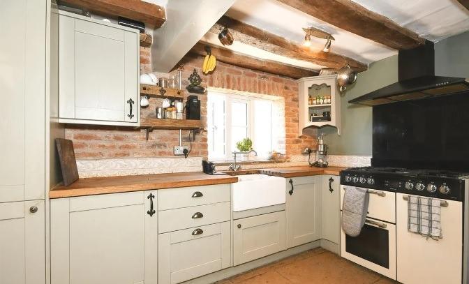 Exposed ceiling beams and brickwork catch the eye in the kitchen which is fitted with storage units and an electric cooker with gas hob.