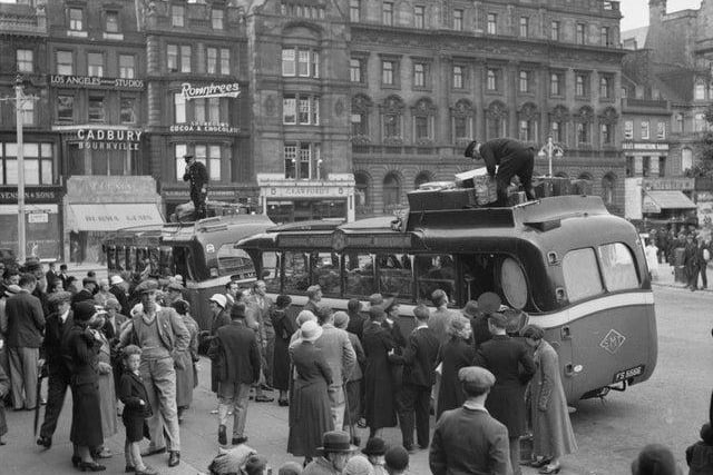 Near the Mound, throngs of passengers wait to board a pair of early SMT ‘luxury’ coaches, one of them London-bound. Holdalls are being secured to the roofs.