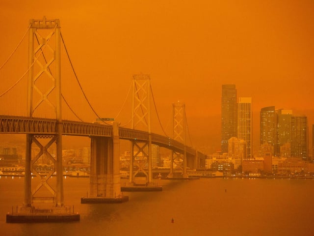 The San Francisco Bay Bridge and city skyline are obscured in orange smoke.