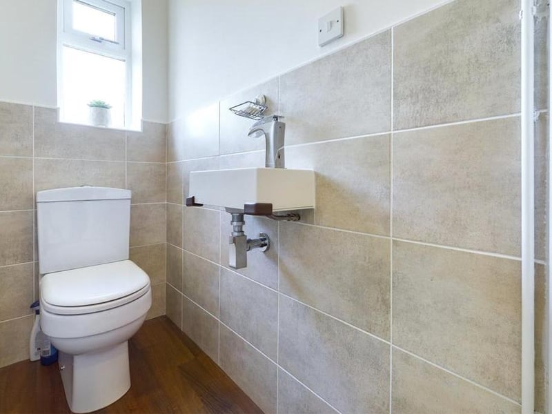 Cloakroom - Modern white suite cloakroom suite comprising low level WC and wall mounted wash basin; wood effect laminate flooring, uPVC double glazed window and radiator panel.
