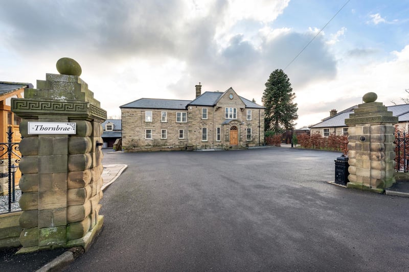 The house is approached via a beautiful stone pillared entrance, with decorative wrought iron railings and a stone wall, leading to an extensive tarmac driveway area with parking for several cars.