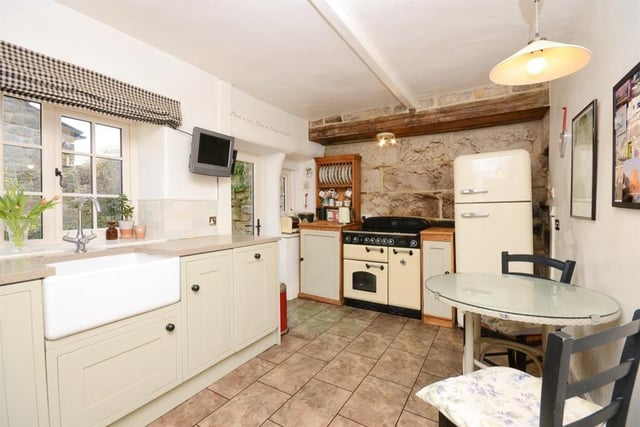 The colours in  the exposed stonework on one wall are reflected in the floor tiles of the kitchen which has a Belfast sink inset within the hand-painted units.