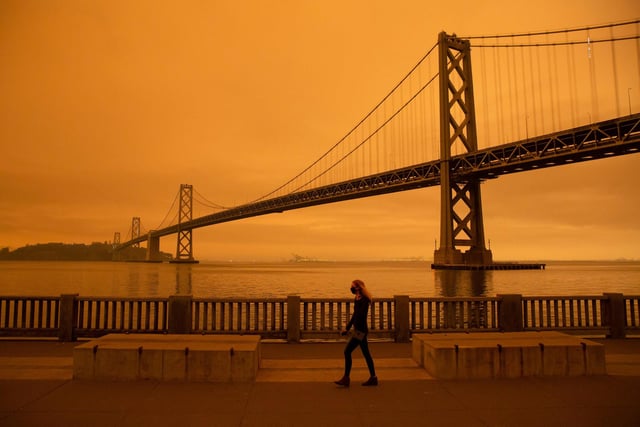 A woman walks along The Embarcadero under an orange smoke-filled sky in San Francisco.